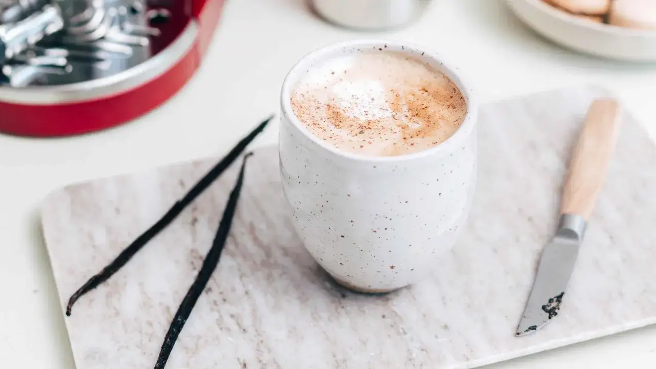 En kr&auml;mig vaniljlatte hemma, med vaniljst&auml;nger och en liten kniv p&aring; en marmorplatta.