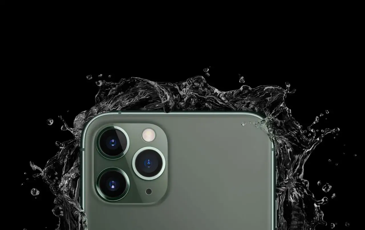 El iPhone 11, con sus c&aacute;maras de 12 megap&iacute;xeles, resiste salpicaduras de agua en un fondo negro.