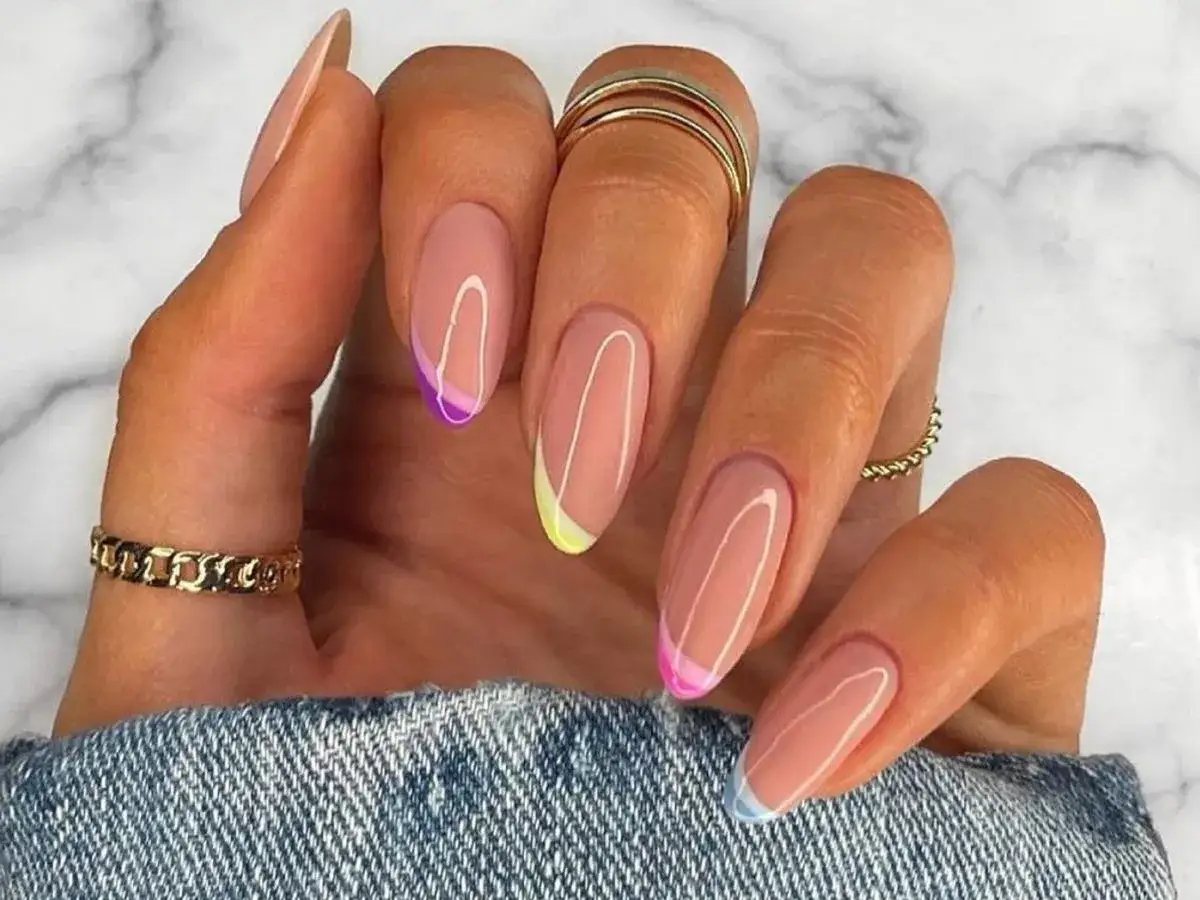 Dłonie z paznokciami w stylu french nails, ozdobione kolorowymi końcówkami: fioletową, żółtą, różową i błękitną.