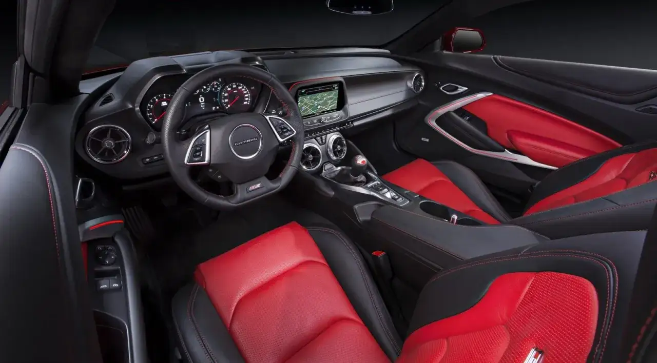 Wnętrze Chevrolet Camaro z czerwono-czarną tapicerką, sportową kierownicą i ekranem nawigacji.