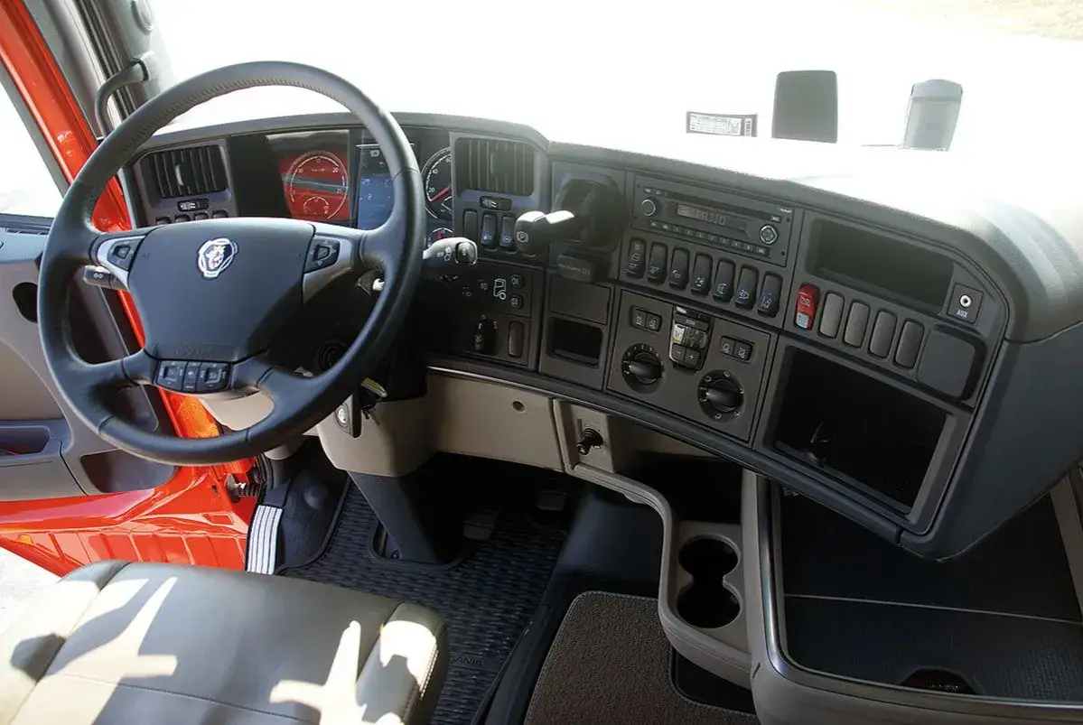 Wnętrze kabiny ciężarówki Scania R z kierownicą, deską rozdzielczą i radiem.