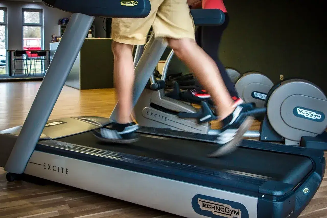 Osoba ćwiczy na bieżni Technogym, aby schudnąć. Szybki ruch nóg sugeruje intensywny trening.