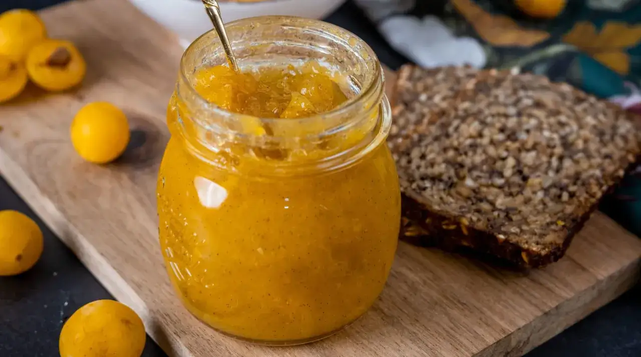 Ein Glas mit raffinierter Mirabellenmarmelade, daneben ein St&uuml;ck Vollkornbrot und frische Mirabellen.