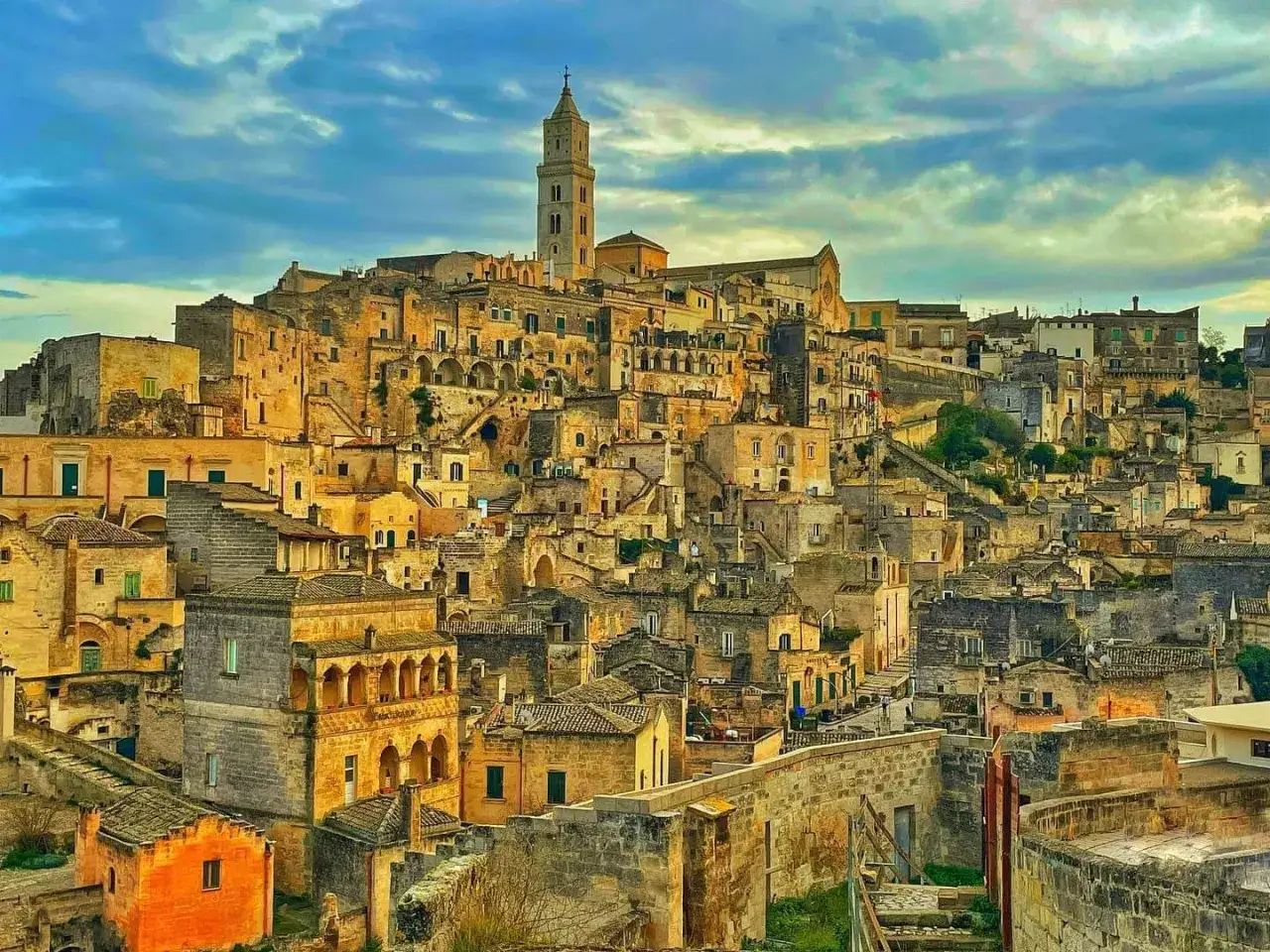 Matera, najstarsze miasto we Włoszech, z kamiennymi domami wciśniętymi w zbocze wzgórza i wieżą kościelną górującą nad krajobrazem.
