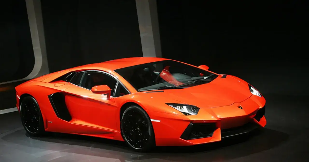 Pomarańczowy Lamborghini Aventador z czarnymi felgami, prezentowany na ciemnym tle.
