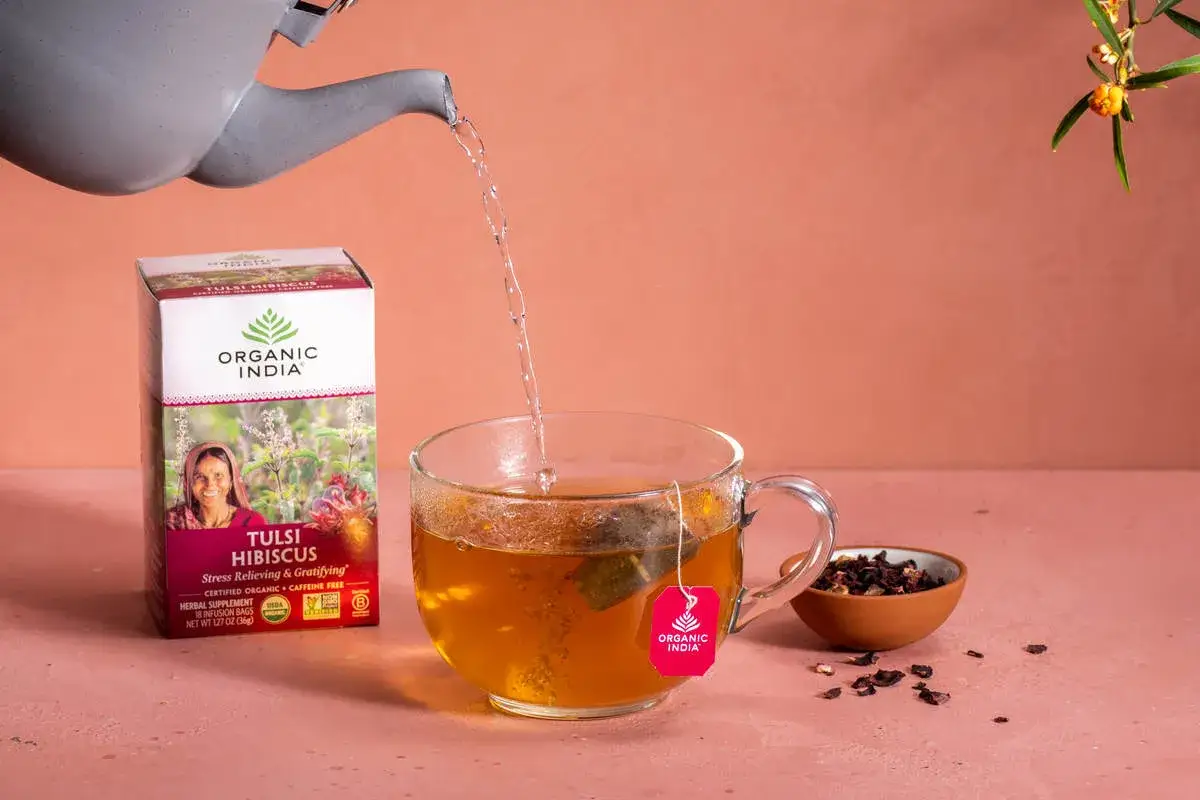 Agua caliente se vierte en una taza de té de flor de jamaica, junto a una caja de té.