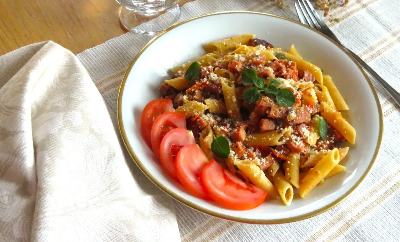 En tallrik med penne pasta i en smakrik skinksås, toppad med riven ost och färska örter. Serveras med skivade tomater.