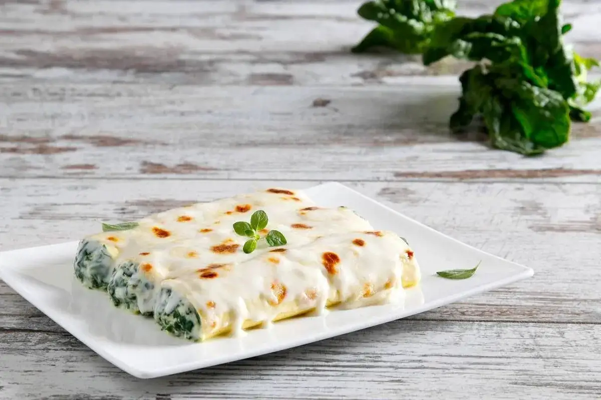 Cannelloni ricotta e spinaci fumanti, ricoperti da besciamella dorata e guarniti con un rametto di origano fresco.