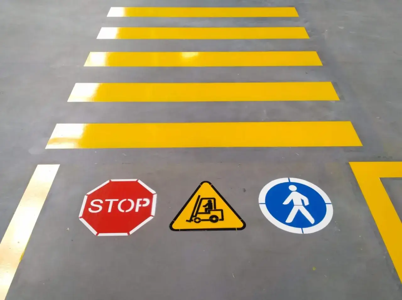 Oznakowane drogi transportowe w magazynie: pasy dla pieszych, znak STOP, ostrzeżenie o w&oacute;zku widłowym i ścieżka dla pieszych.