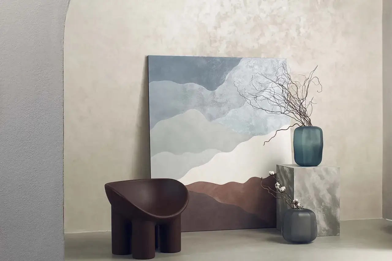 Un soggiorno moderno con un quadro astratto che evoca paesaggi montani, una poltrona scultorea e vasi decorativi. I **stili di pittura per interni** si fondono con arredi di design.