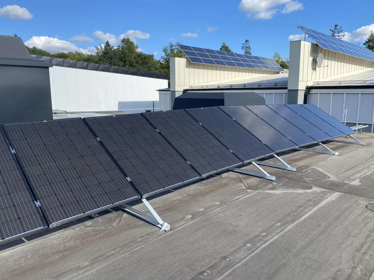 Solceller tak p&aring; en byggnad med bl&aring; himmel och moln. Solpanelerna &auml;r monterade p&aring; taket och f&aring;ngar solens energi.