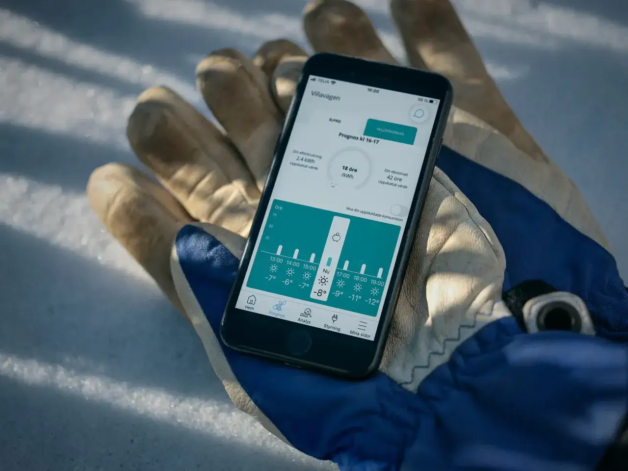 En mobiltelefon visar elpriser och prognoser i elpriskollen appen, placerad på en handske i snön.
