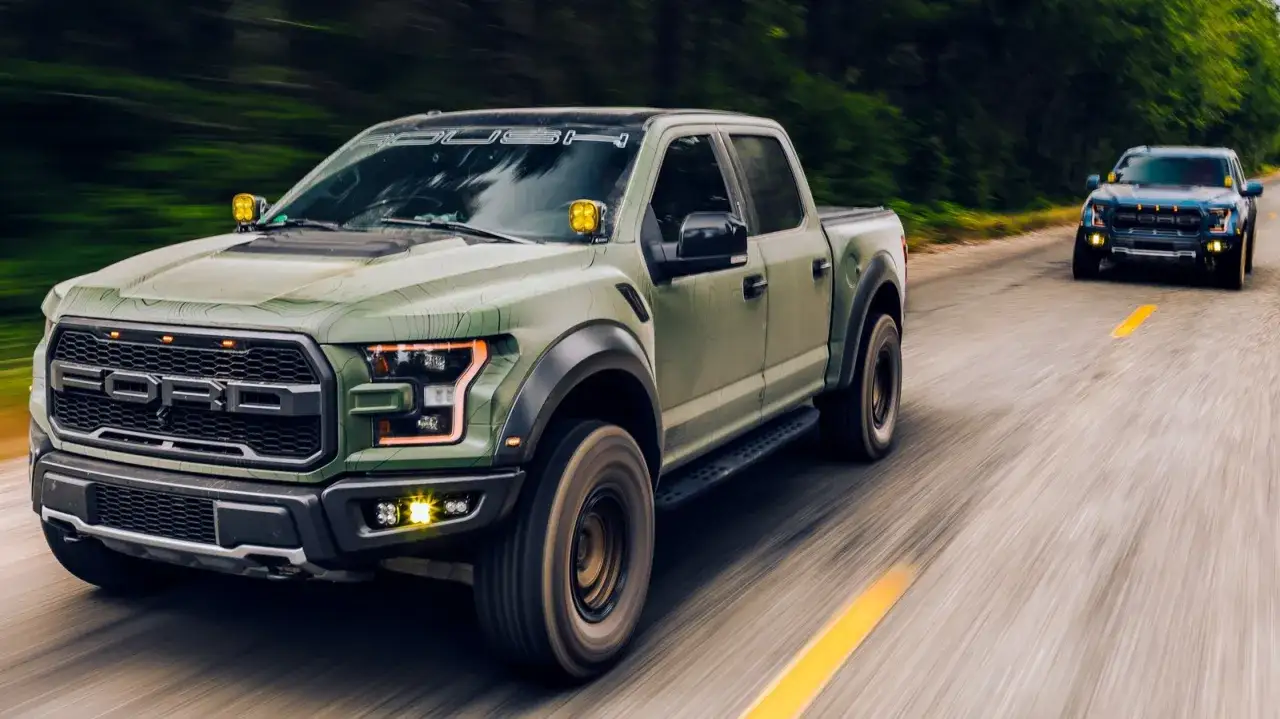 Deux Ford Raptor verts et bleus filent sur une route, le vert &eacute;tant le camion le plus rapide du monde, avec des lumi&egrave;res jaunes sur le capot.