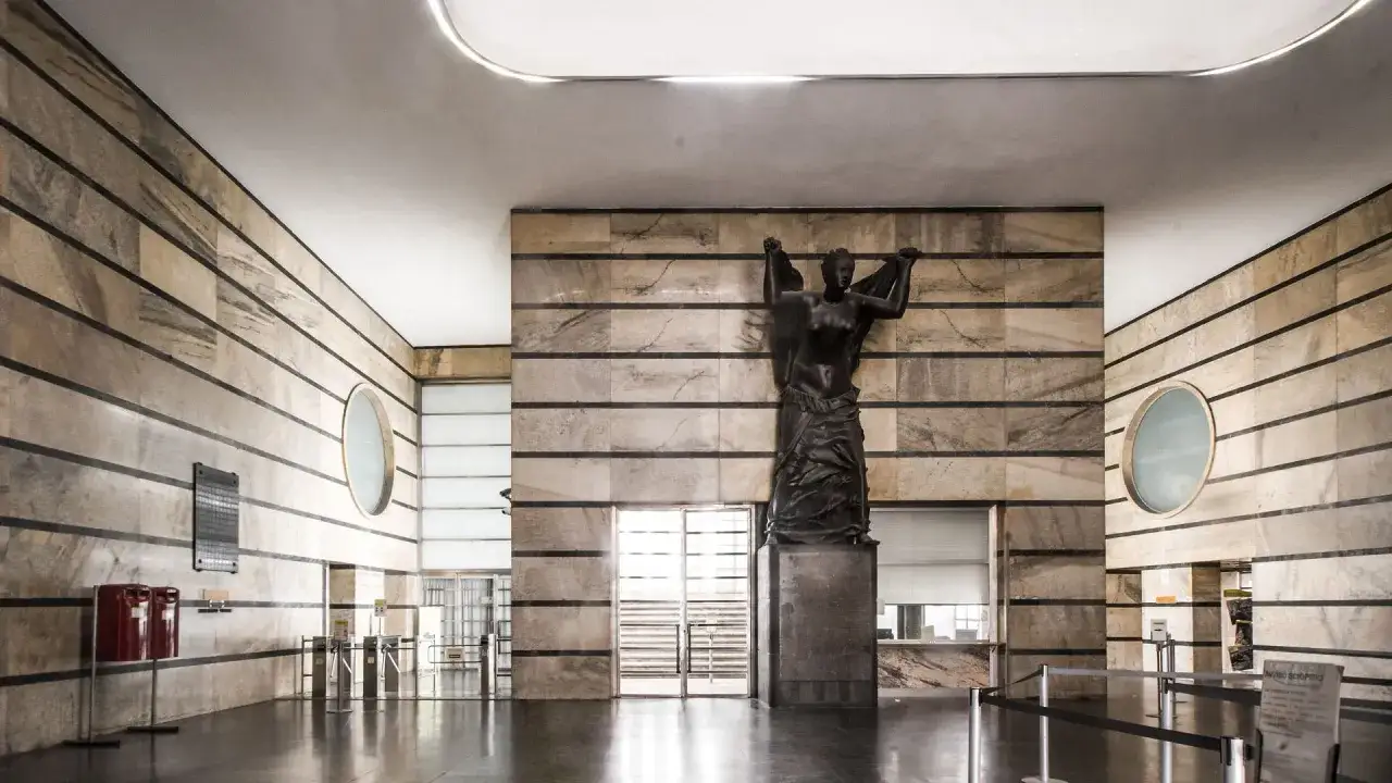 Wnętrze w stylu modernizm co to? Monumentalna rzeźba kobiety na tle marmurowych ścian z czarnymi pasami, okrągłe okna, eleganckie barierki.