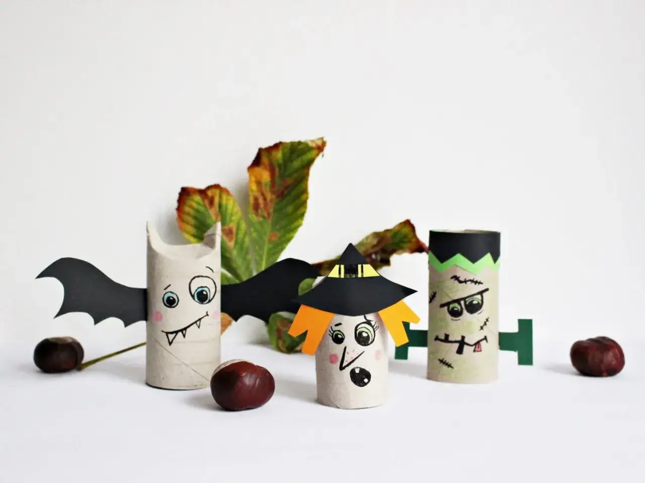 Basteln mit Klopapierrollen für Halloween: Ein Fledermaus-Monster, eine Hexe und Frankenstein mit Kastanien und Herbstlaub.