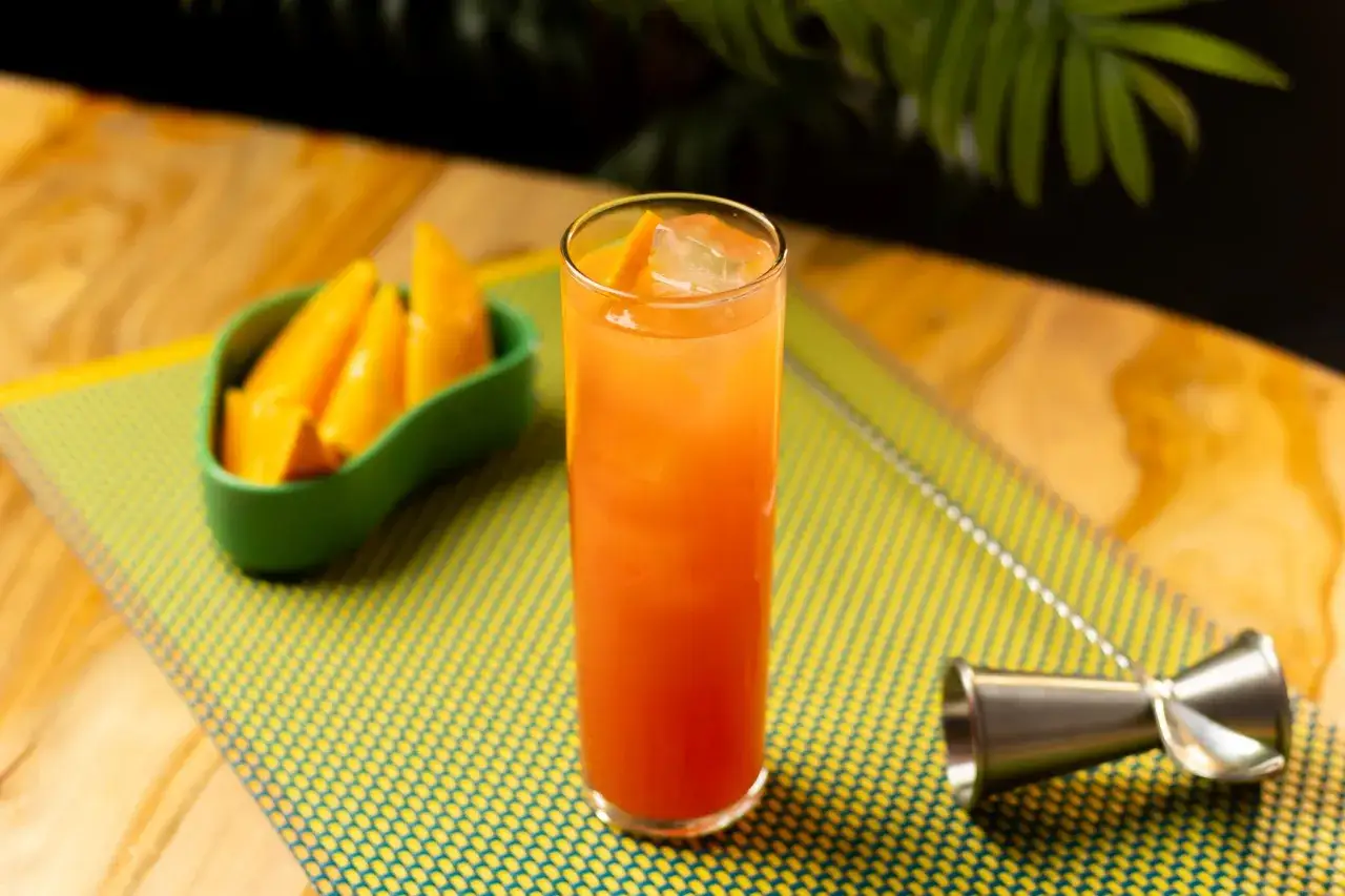 Erfrischender Campari Orange mit Eis und Orangenspalten, daneben eine Schale mit Mangostücken.