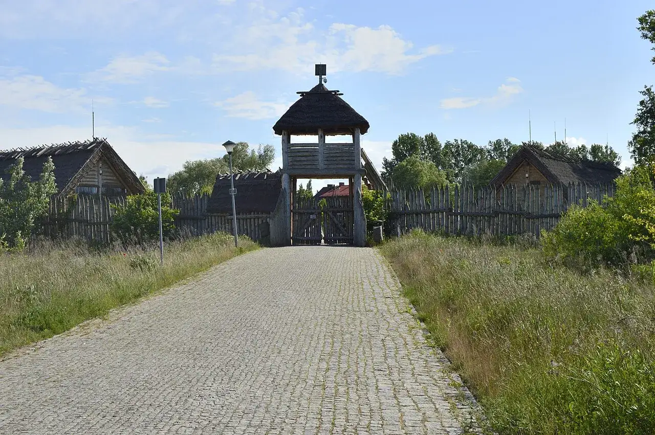 Kamienna droga prowadzi do drewnianej bramy z wieżą. Wok&oacute;ł chaty kryte strzechą i palisada. Pruszcz Gdański atrakcje historyczne.