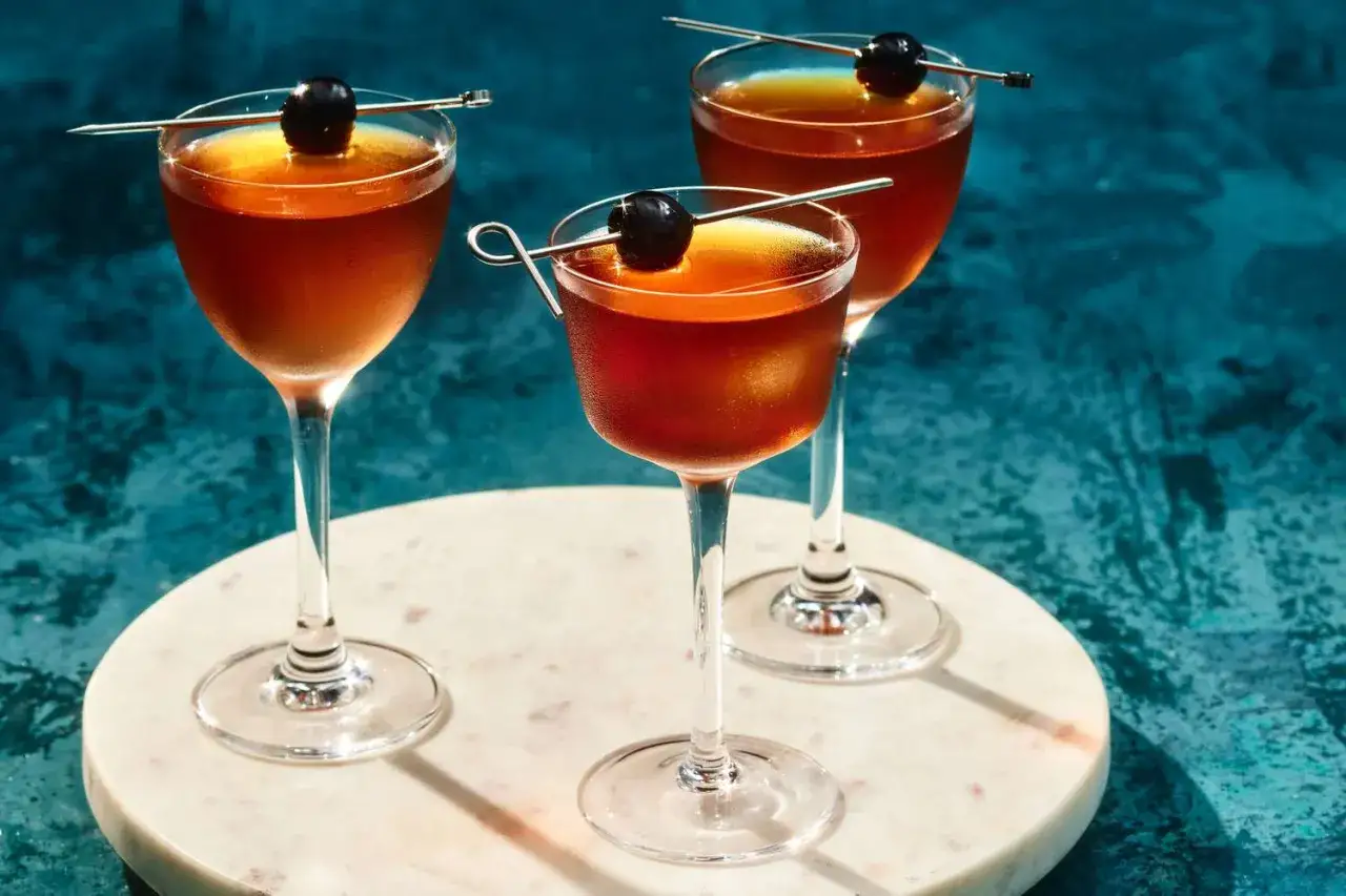 Tre eleganta manhattan drinkar med k&ouml;rsb&auml;r p&aring; cocktailpinnar, serverade p&aring; ett marmorfat.