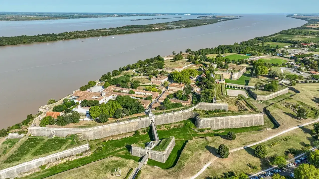 Vista aérea de la ciudadela de Blaye, con sus imponentes murallas y edificios históricos junto a un ancho río.