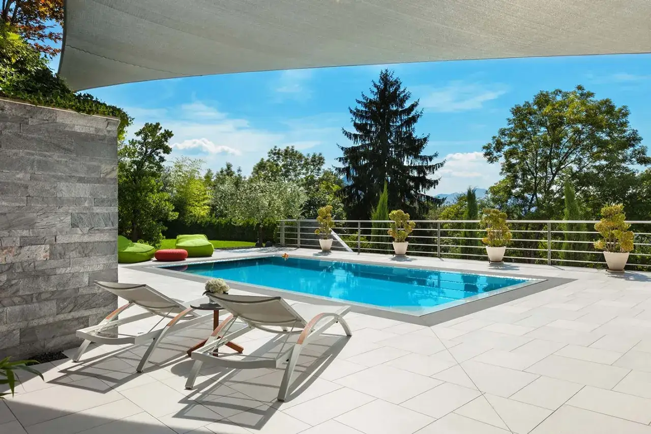 Piscina azzurra con lettini e piante, pronta per l'estate. La manutenzione piscina è fondamentale per godersi questo angolo di paradiso.