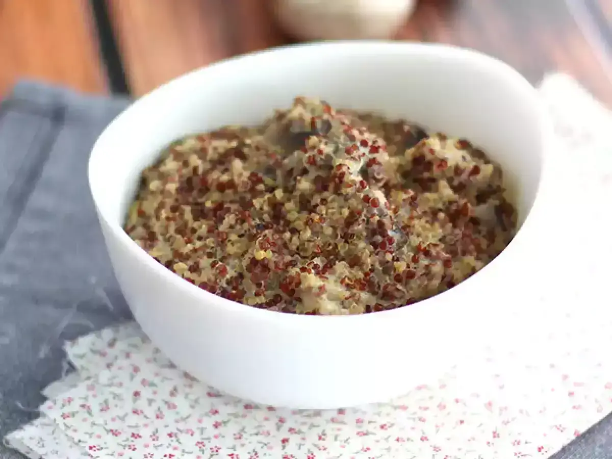 Un bol de risotto de quinoa crémeux, aux grains multicolores, servi sur une serviette à motifs floraux.