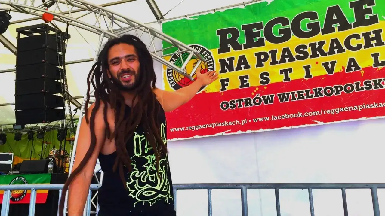 Uśmiechnięty mężczyzna z dredami, członek polskiego zespołu reggae, zaprasza na festiwal.