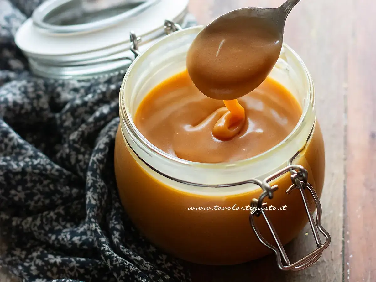 Un cucchiaio raccoglie il cremoso dulce de leche da un barattolo di vetro.
