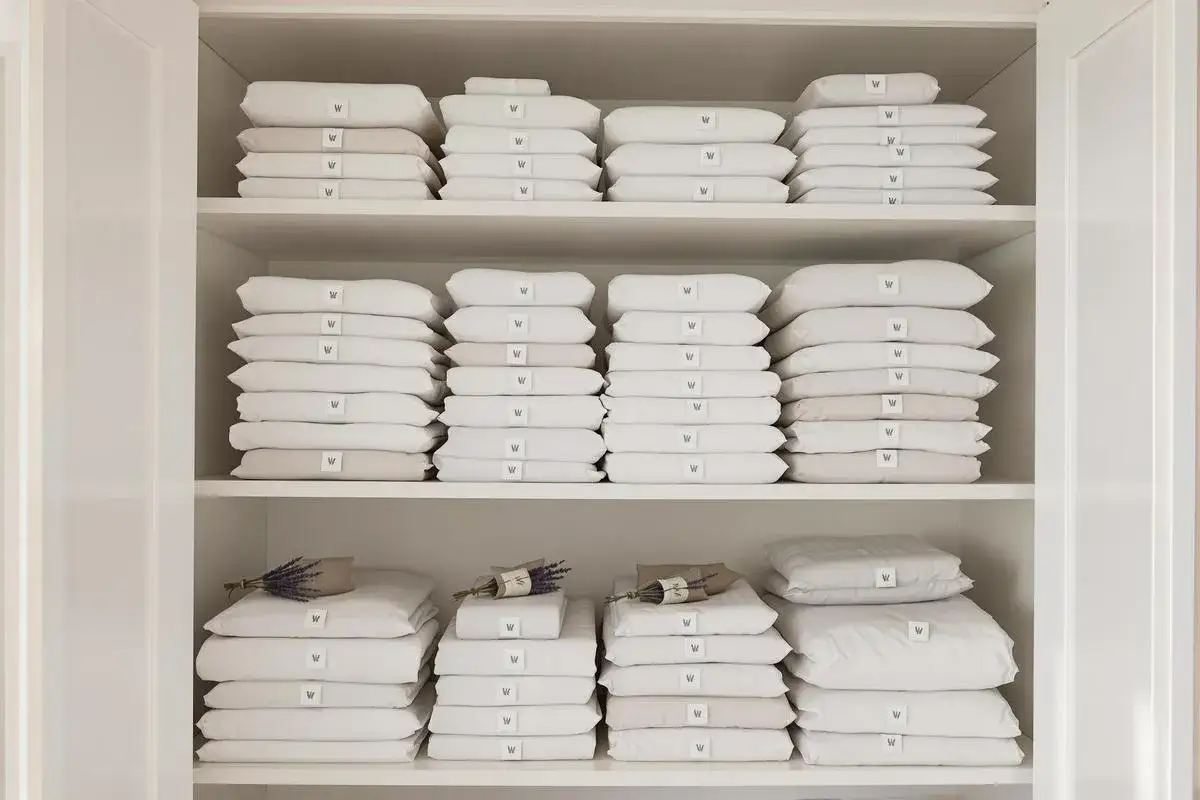 &Eacute;tag&egrave;res remplies de linge de lit blanc et beige pli&eacute;. Une astuce rangement linge de lit pour une organisation parfaite.