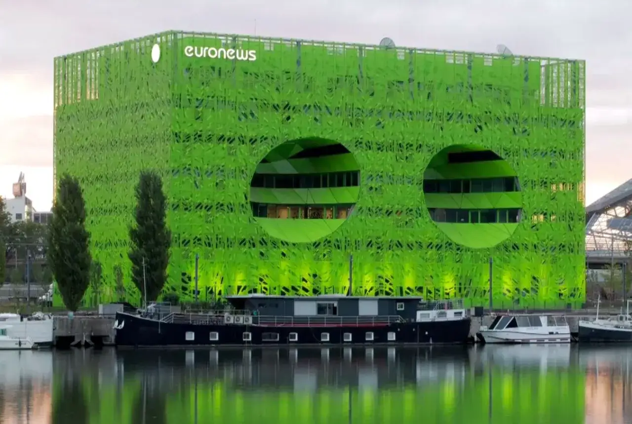 Edifici ecosostenibili con facciata verde brillante e due grandi aperture circolari, riflessi sull'acqua con barche ormeggiate.