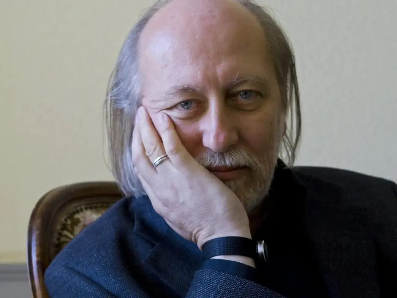 Ritratto pensieroso di László Krasznahorkai, con la mano sul viso e lo sguardo intenso.