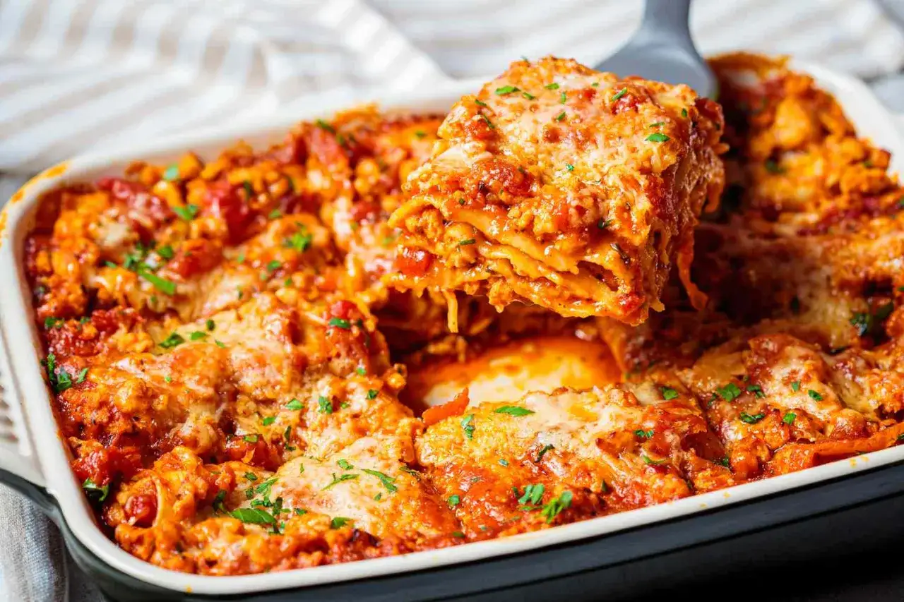 Una porción de lasaña de carne recién horneada, con capas de pasta, salsa de tomate y queso derretido, es servida de una bandeja.