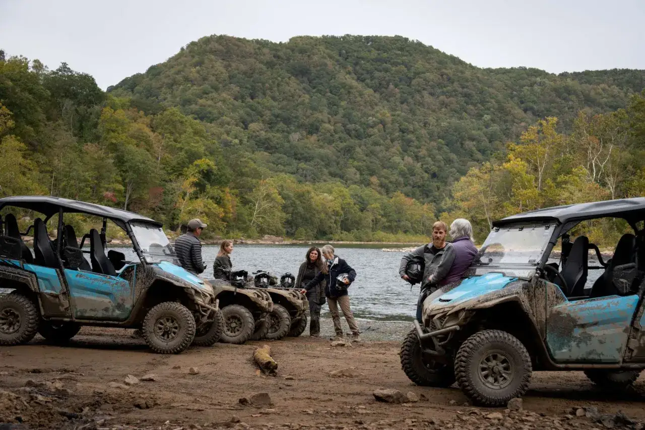 Grupa ludzi przy quadach Polaris nad jeziorem, gotowa na przygodę i **polaris camping**. Malowniczy krajobraz jesienny.
