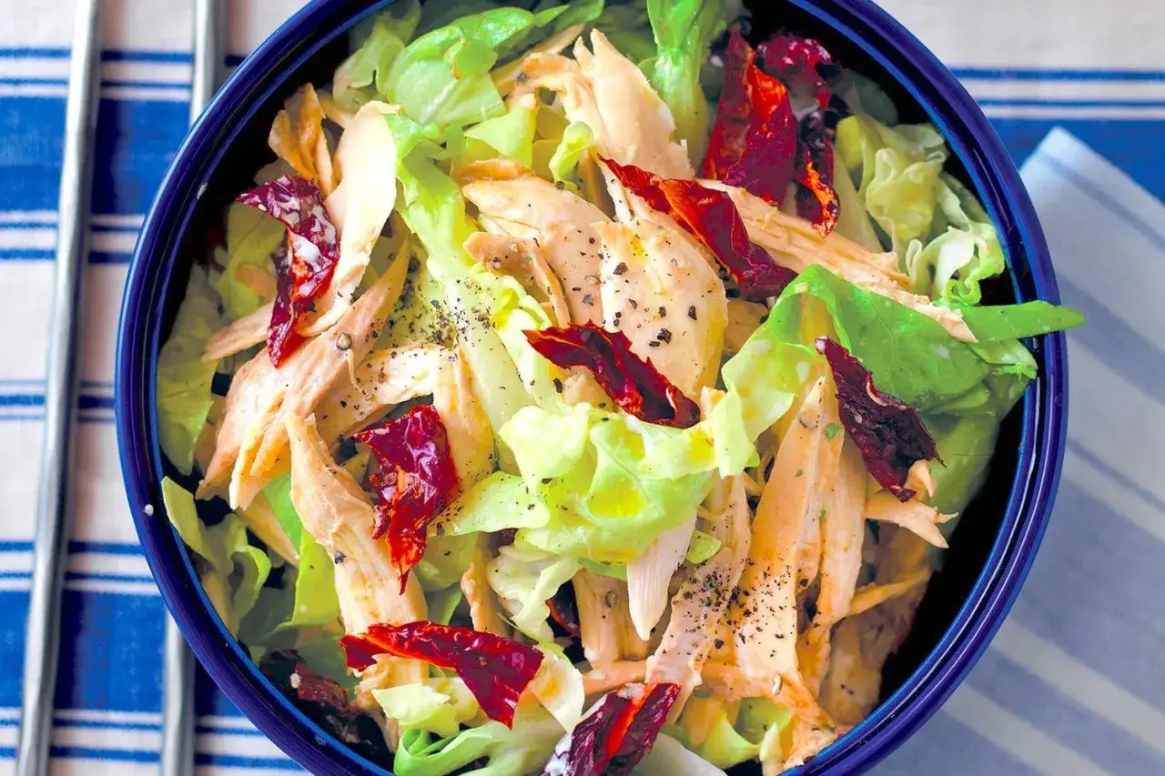 Insalata di pollo sfilacciato con lattuga croccante e pomodori secchi, condita con pepe nero.