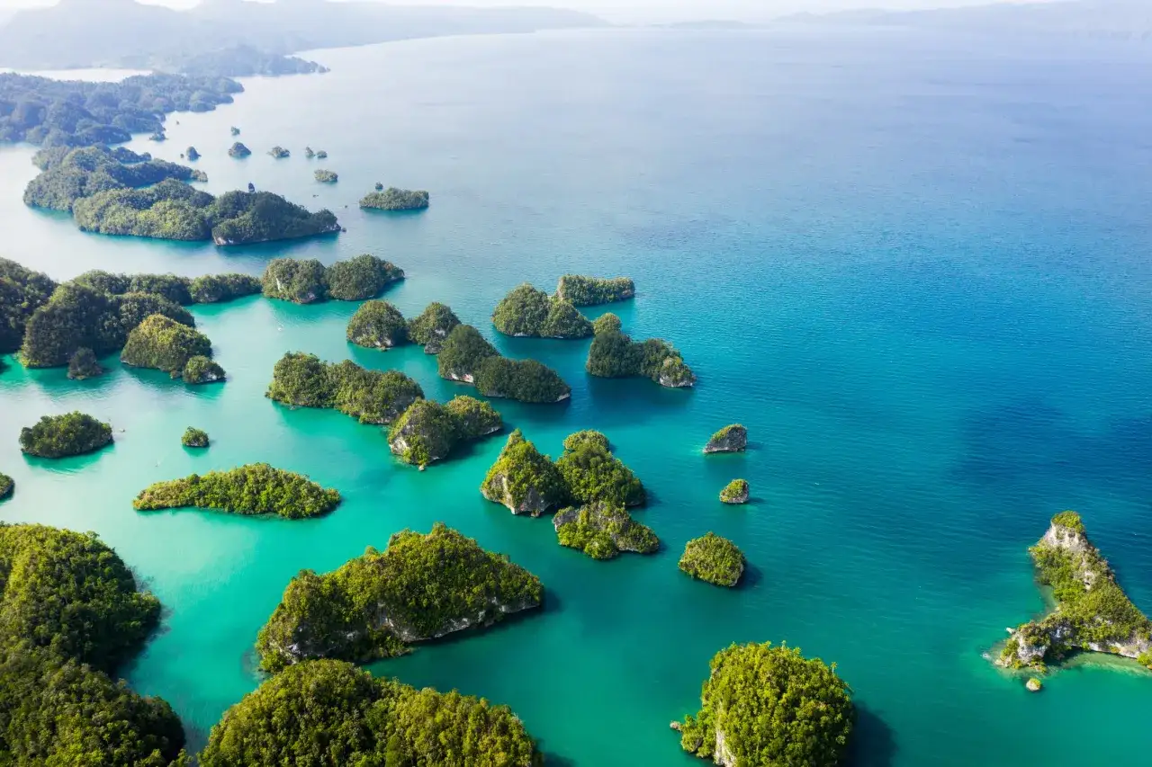 Rajskie widoki z lotu ptaka na archipelag zielonych wysepek w Indonezji. Turkusowa woda otacza liczne, porośnięte bujną roślinnością skaliste wysepki.