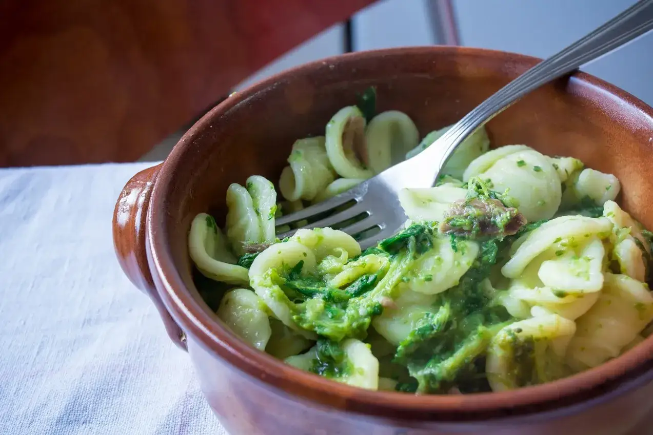 Orecchiette con cime di rapa, uno dei piatti tipici foggiani, servite in una ciotola di terracotta con una forchetta.