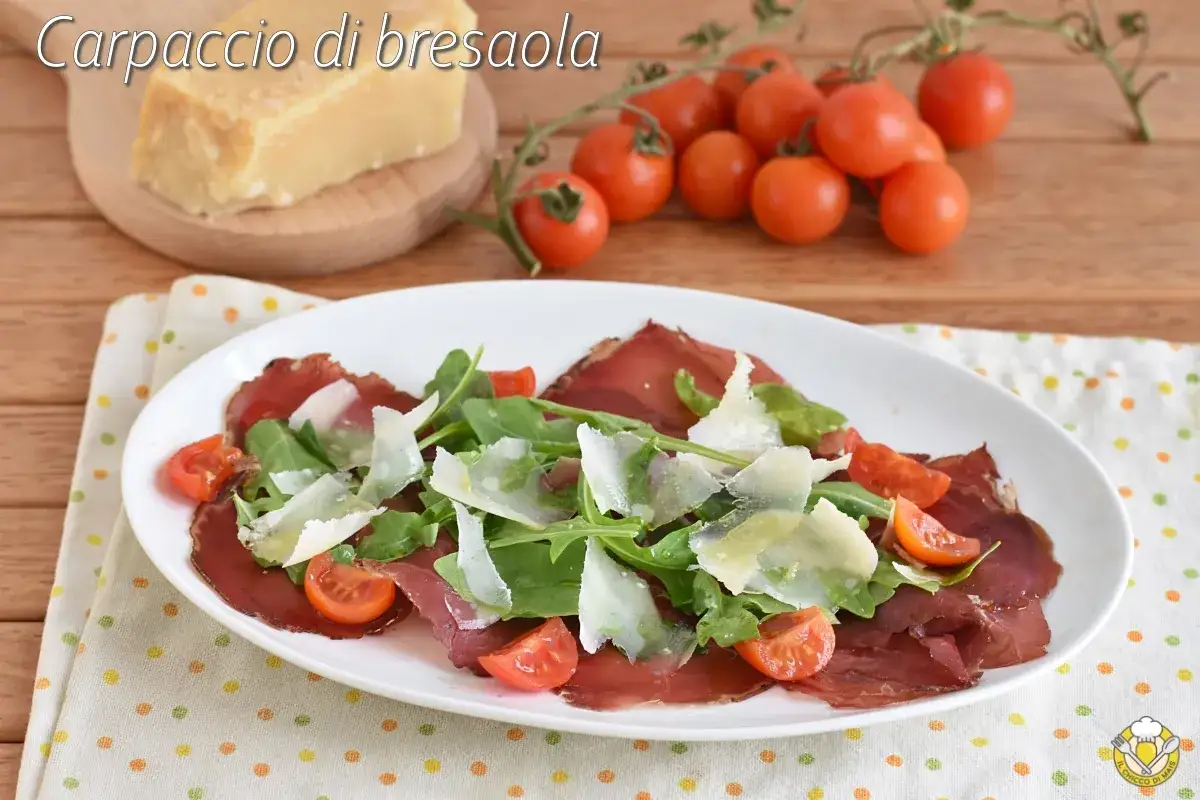 Carpaccio di bresaola rucola e grana, un piatto fresco e saporito con pomodorini e scaglie di Parmigiano Reggiano.