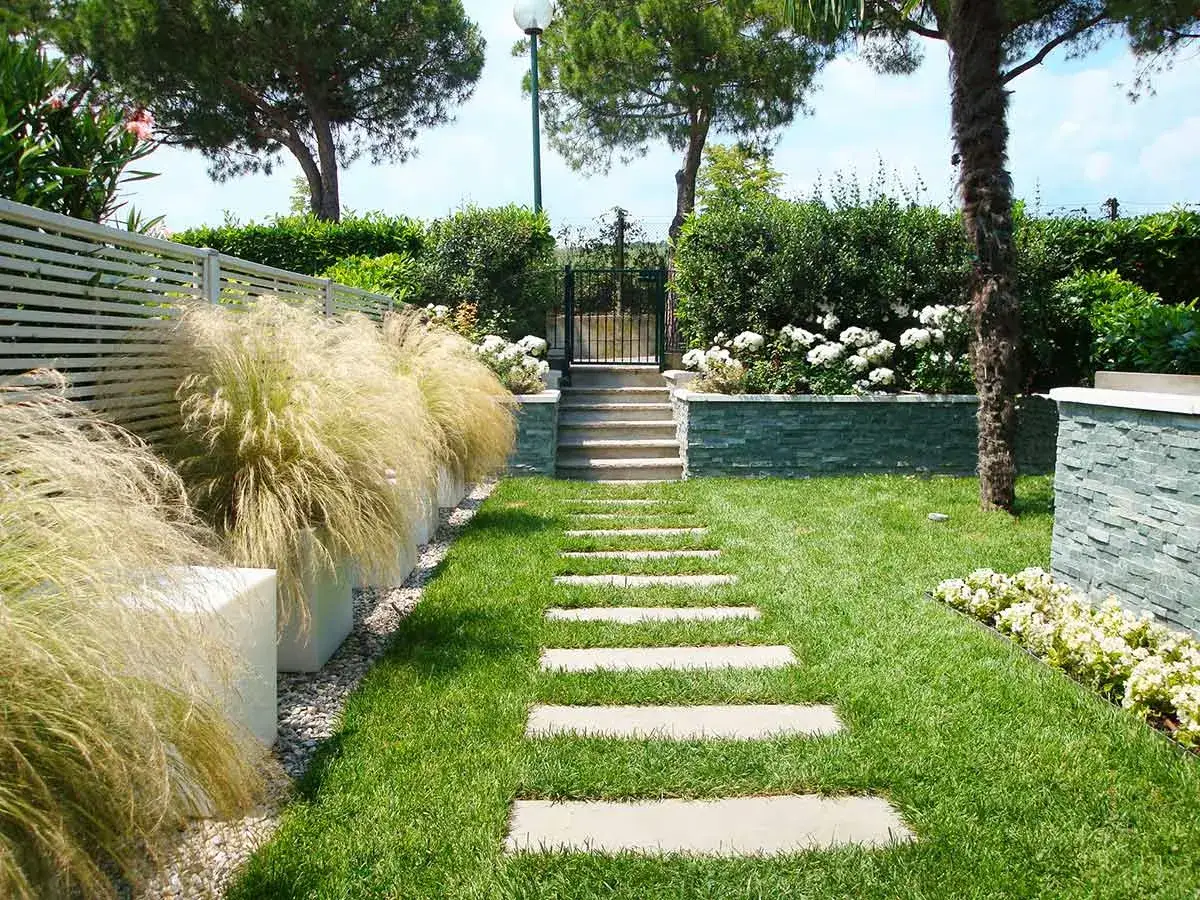 Percorso in pietra per un giardino piccolo moderno, con erba ornamentale e aiuole fiorite.