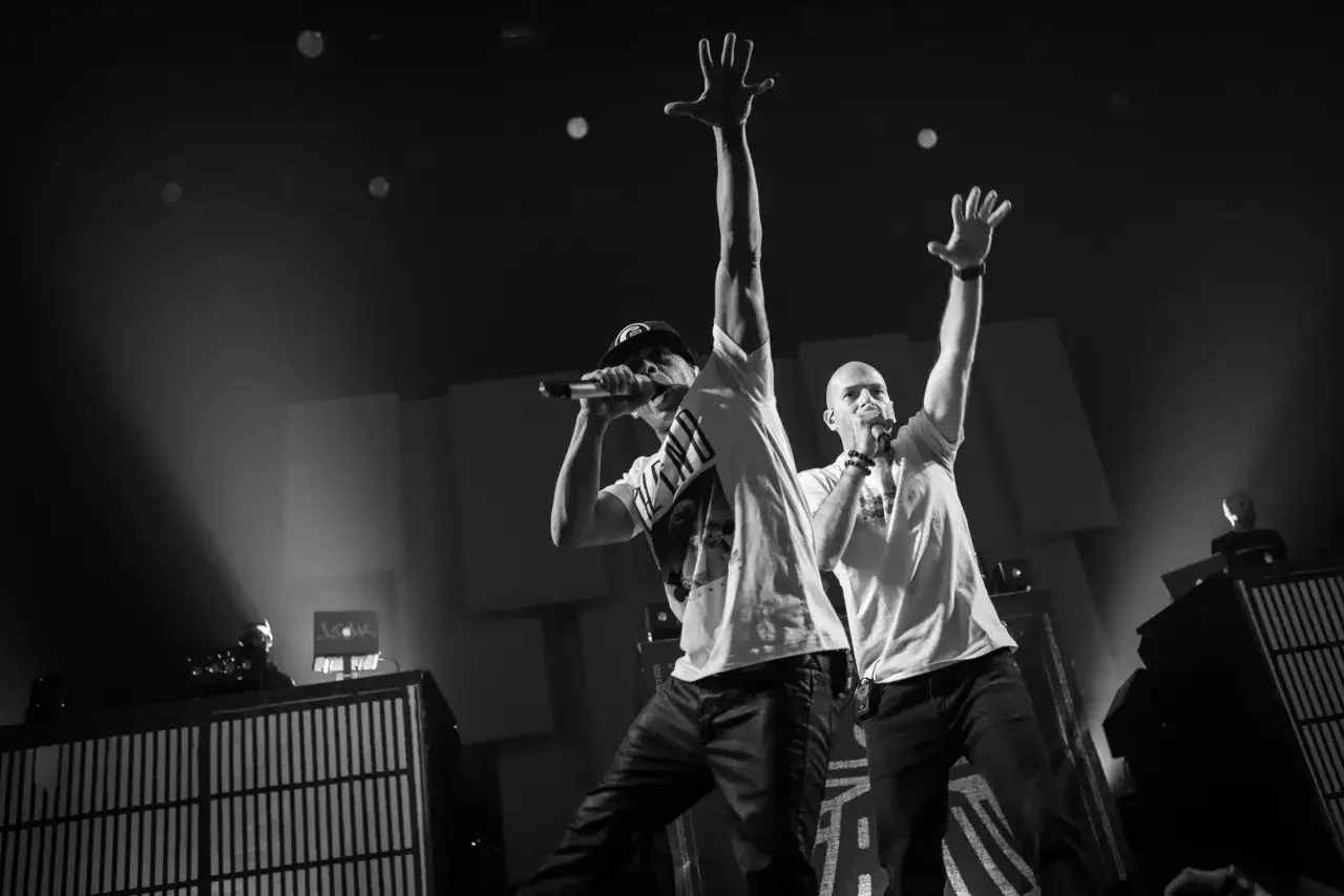 Deux chanteurs rap fran&ccedil;ais sur sc&egrave;ne, micro en main, bras lev&eacute;s vers le ciel, dans une ambiance &eacute;lectrique.