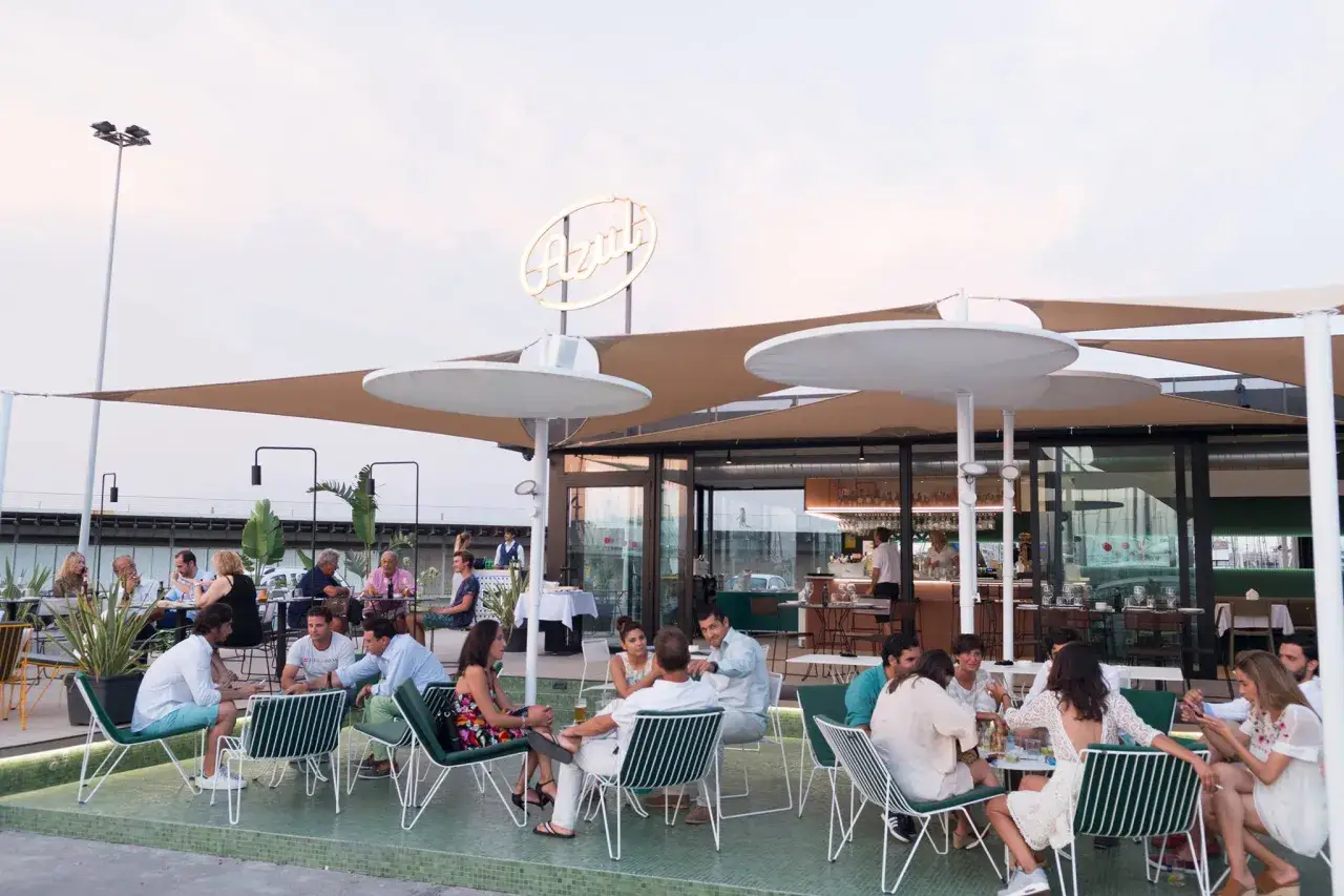Gente disfrutando en terraza de restaurante con letrero
