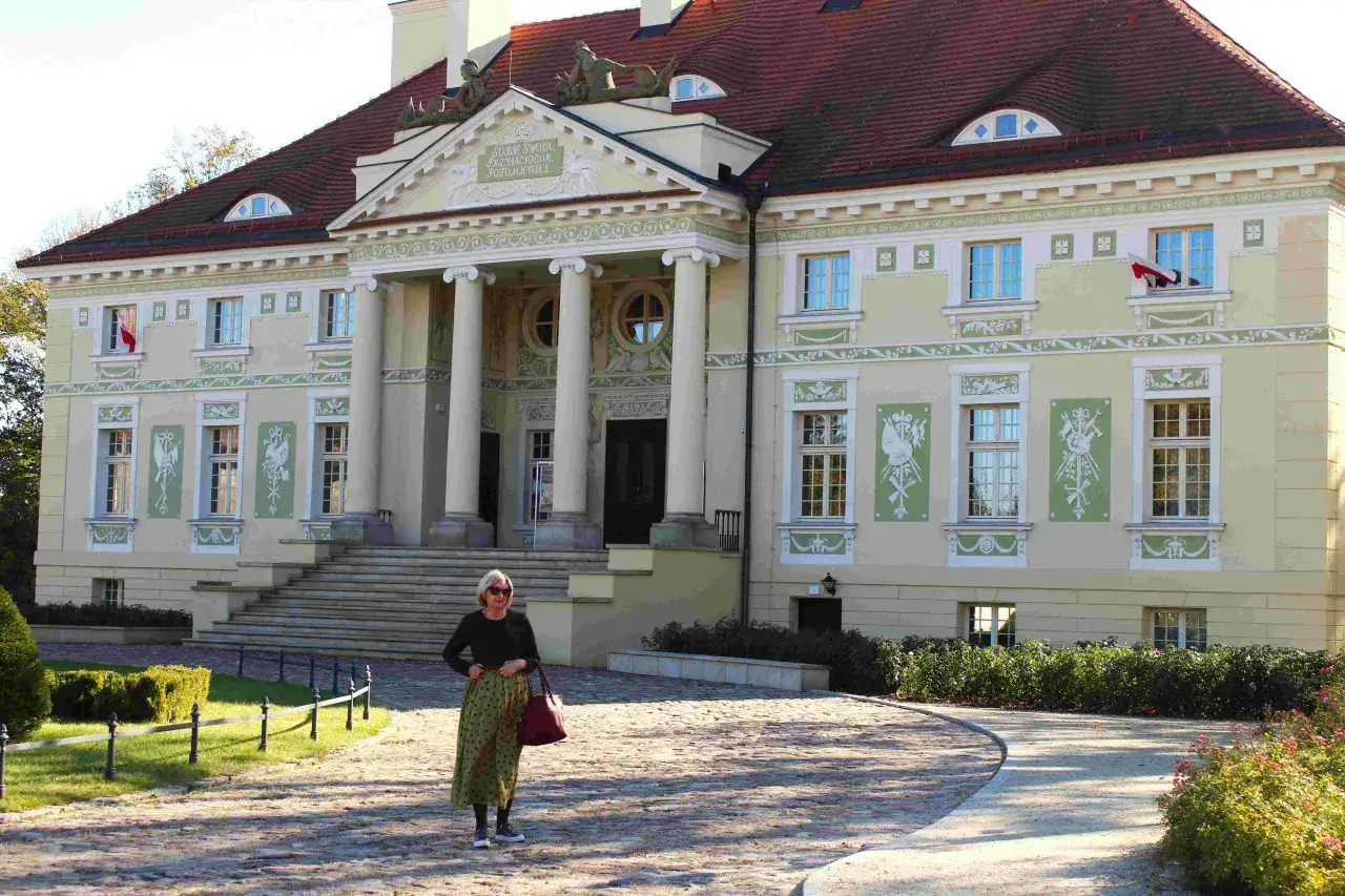 Elegancka kobieta na tle pałacu w stylu neoklasycyzmu. Monumentalna fasada z kolumnami i ozdobnymi detalami architektonicznymi.