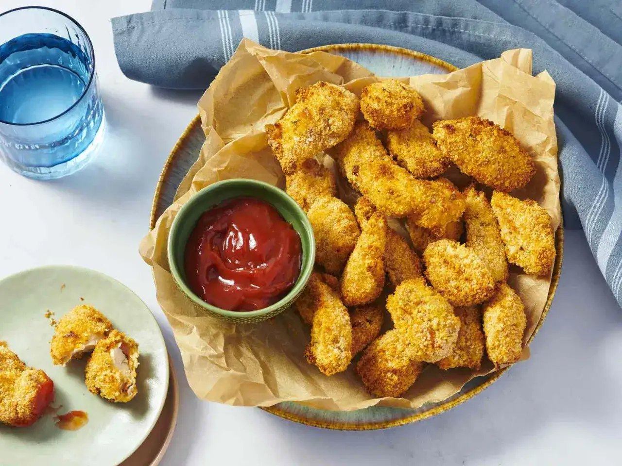 En tallrik med gyllene, krispiga chicken nuggets, en skål ketchup och ett glas vatten. Perfekt för en snabb och god måltid.
