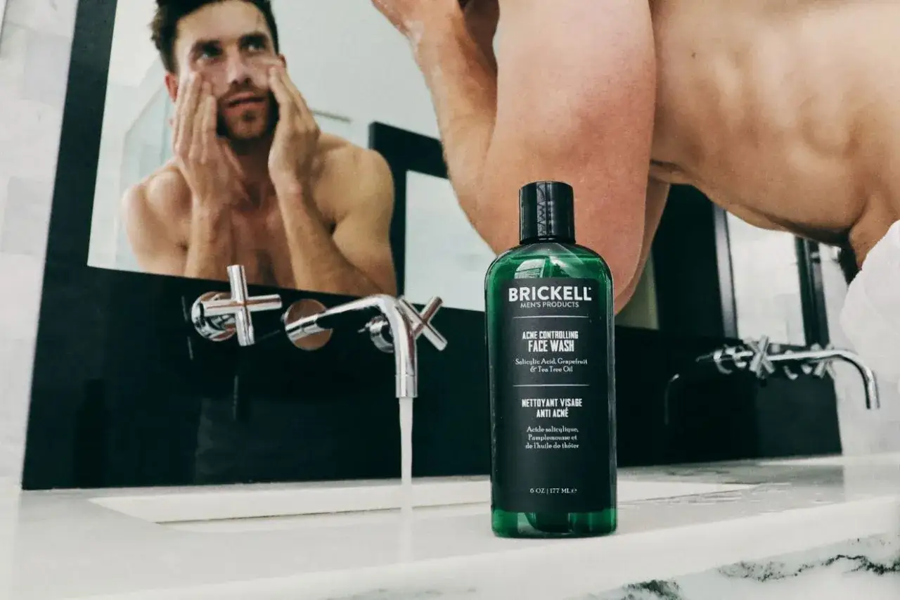 Hombre lav&aacute;ndose la cara frente al espejo, con un limpiador facial anti-acn&eacute; para combatir los granos en la barbilla.