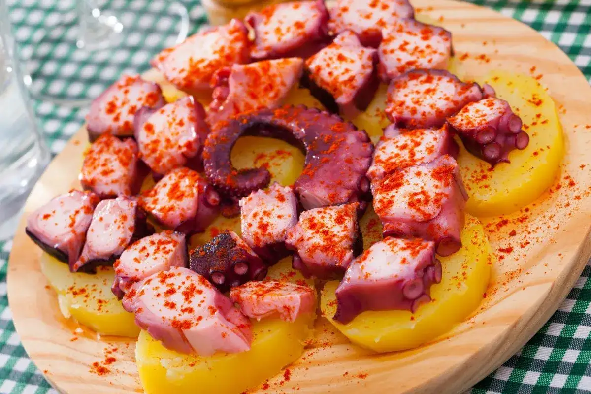 Un plat de poulpe &agrave; la gallega, des morceaux de poulpe tendres et des rondelles de pommes de terre, saupoudr&eacute;s de paprika, sur une planche en bois.