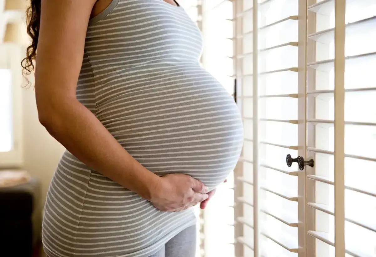 Frau im 38. SSW h&auml;lt ihren runden Bauch. Das gestreifte Kleid betont die Schwangerschaft.