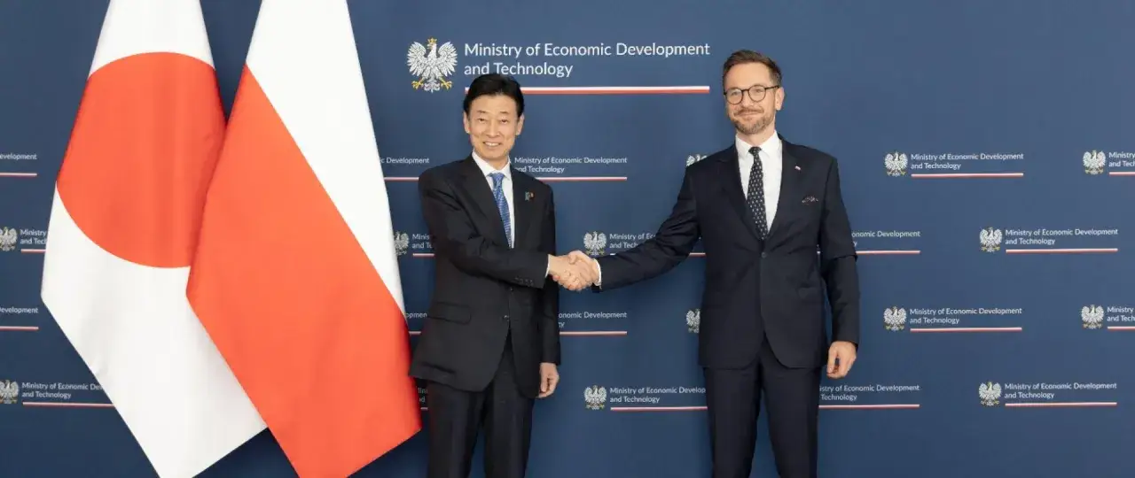Polska i Japonia zacieśniają więzi. Dwóch mężczyzn w garniturach ściska sobie dłonie na tle flag obu krajów.