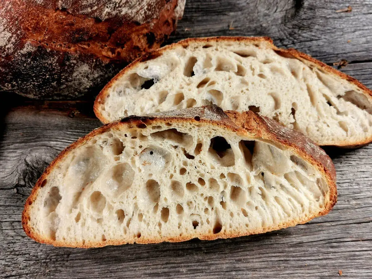 Zwei Scheiben rustikales Sauerteigbrot mit gro&szlig;er Krume liegen auf Holz. Die Sauerteig Vorteile sind die tolle Textur und der Geschmack.