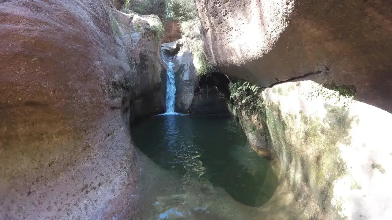 Cascada y poza natural en el gorg de la Mola, rodeado de rocas erosionadas y vegetaci&oacute;n.