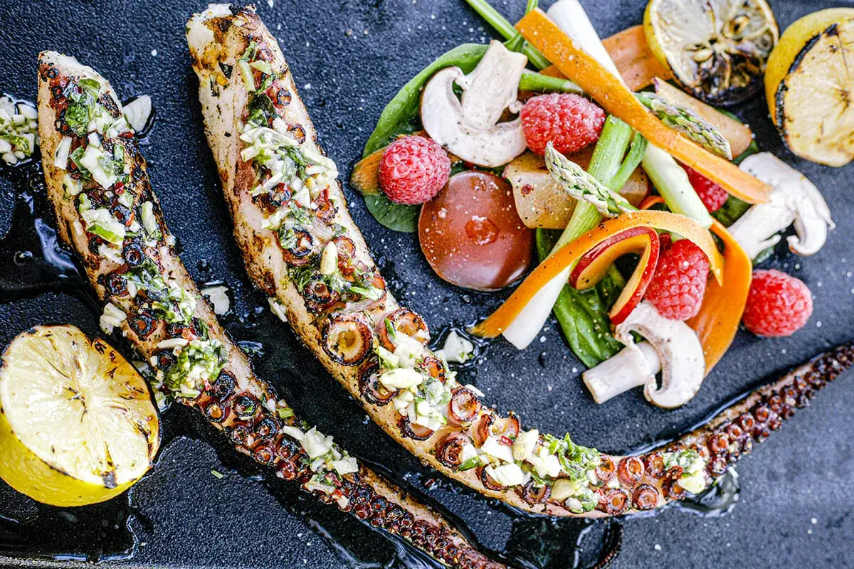 Tentacules de poulpe au barbecue, grillés et garnis d'herbes fraîches, servis avec des légumes croquants et des quartiers de citron grillé.
