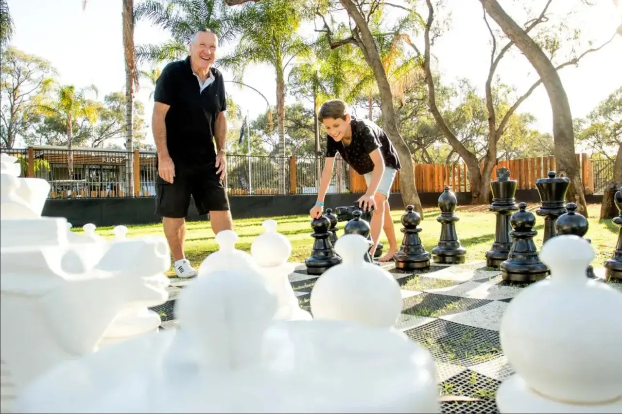 Abuelo y nieto jugando ajedrez gigante al aire libre, un momento para disfrutar en familia.
