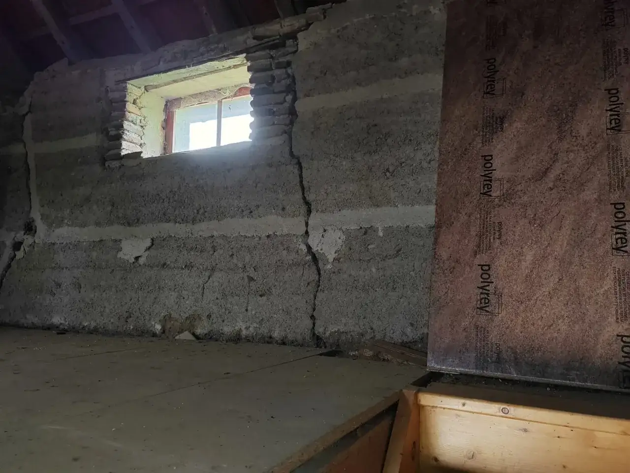 Intérieur d'une grange en pierre avec une fissure visible, une fenêtre et des panneaux de protection. Un projet de budget rénovation maison à prévoir.